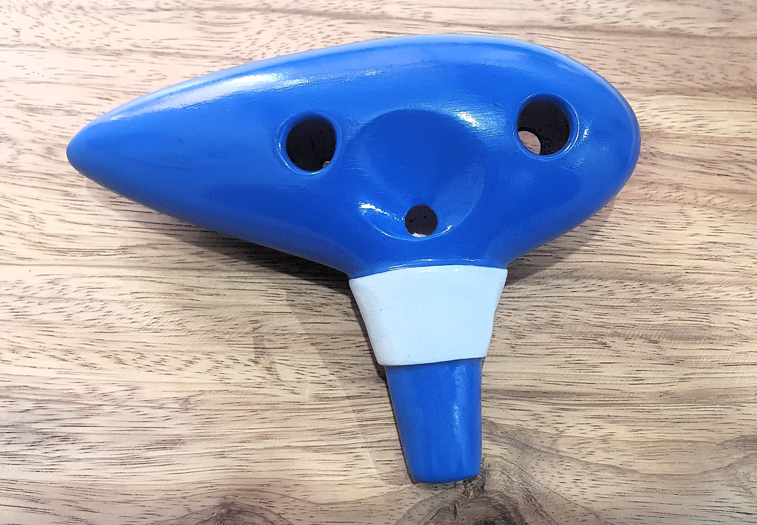 Foto da visão trazeira de uma ocarina de 12 furos de cor azul e com símbolo do The Legend of Zelda: Ocarina of Time.