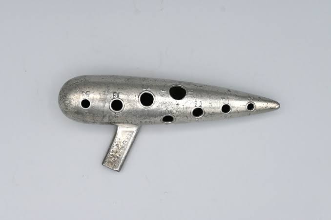Ocarina de metal lisa, com emboradura lateral ligeiramente recurvada para a esquerda.