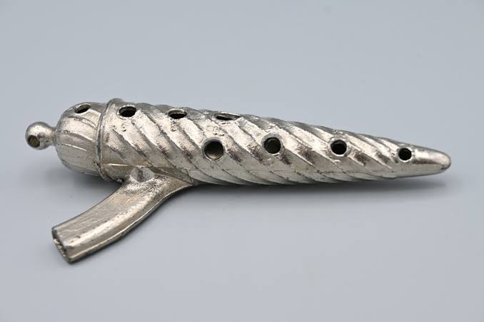 Ocarina de metal com estrias, deslgada em formato de um torpedo com uma embocadura ligeiramente recurvada para a esquerda.