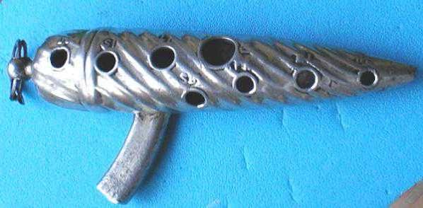 Ocarina de metal com estrias, deslgada em formato de um torpedo com uma embocadura ligeiramente recurvada para a esquerda.